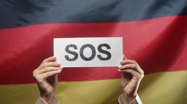 SOS, alarm, Deutschland bayrağı geçmişinde acil durum kartı olan kadın eller. İşçi sömürüsü, göçmenler, mülteciler, insan kaynakları, yardım talebi, çevre bakımı. Yüksek kalite