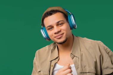 Olumlu melez ırkçı müzik dinliyor, yeşil stüdyo arka planında modern kulaklıklarla dansın tadını çıkarıyor. Radyo, kablosuz modern ses teknolojisi, çevrimiçi çalar. Yüksek kalite