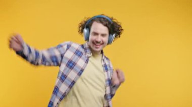 Pozitif beyaz Avrupalı adam müzik dinliyor, sarı stüdyo arka planında modern kulaklıklarla dans ediyor. Radyo, kablosuz modern ses teknolojisi, çevrimiçi çalar. Yüksek kalite 4k