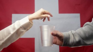 Zengin İsviçreli Kadın İsviçre bayrağında sadaka isteyen evsiz bir adamın plastik bardağına bozuk para atıyor. Paylaşmak ve birbirimize yardım etmek. Yoksul hayat, işsizlik, yoksulluk sınırının altındaki insanlar. 4k görüntü
