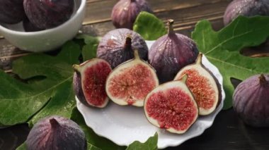 Beyaz tabakta yaprakları olan taze incir, kırsal ahşap masa. Ficus carica. Güzel mevsimlik meyveler, vejetaryen yemekleri. Üst Manzara. Dolly kaydırma atışı. Yüksek kalite 4k görüntü