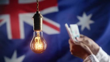 Avustralya Bayrak Arkasında Parlayan Edison Ampulü. Avustralya 'da dolar sayan bir kadın. Elektrik fiyatları, faturalar, enerji krizi, vergi artışı, elektrik faturaları. Yüksek kalite 4k görüntü