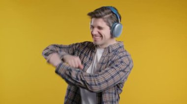 Pozitif beyaz Avrupalı adam müzik dinliyor, sarı stüdyo arka planında modern kulaklıklarla dans ediyor. Radyo, kablosuz modern ses teknolojisi, çevrimiçi çalar. Yüksek kalite 4k