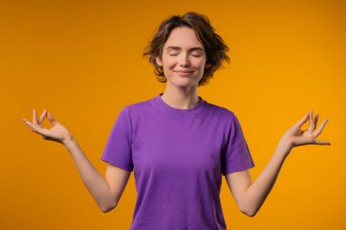 Sakin kadın rahatlıyor, meditasyon yapıyor, stresi reddediyor. Kadın derin nefes alıyor, sarı stüdyo arka planını sakinleştiriyor. Yoga, ahlaki denge, zen konsepti. Yüksek kalite