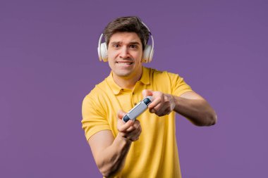 Televizyonda video oyunu oynayan yakışıklı genç adam Violet stüdyosunun arka planında joystick izole edilmiş. Modern teknolojiyi kullanarak.