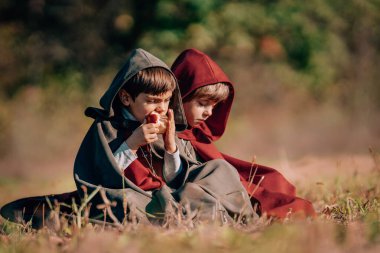 Hobbits boys in costumes sitting on autumn ground to eat apples. Fantasy journey, halloween, fellowship cosplay. High quality  clipart