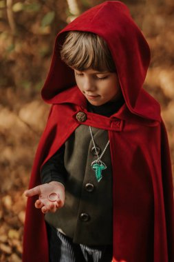 Little cosplayer hobbit boy in cape costume in autumn forest admiring gold ring. Fantasy journey, halloween, fellowship cosplay. High quality clipart