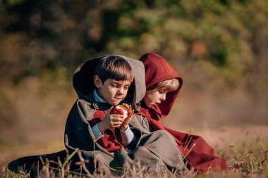 Hobbits boys in costumes sitting on autumn ground to eat apples. Fantasy journey, halloween, fellowship cosplay. High quality  clipart