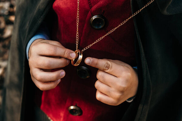 Unrecognizable child cosplayer in hobbit cape costume holding and admiring golden ring. Fantasy journey, halloween, fellowship cosplay. High quality