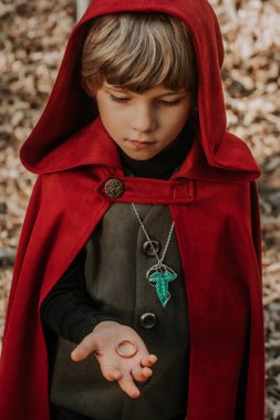 Little cosplayer hobbit boy in cape costume in autumn forest admiring gold ring. Fantasy journey, halloween, fellowship cosplay. High quality clipart