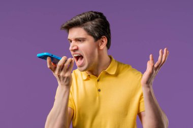 Annoyed young man quarreling while talking on mobile phone. Angry dude, stress. violet studio background. Conflict, dispute, negative. High quality  clipart