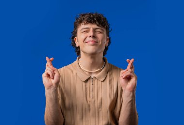 Genç adam mavi arka planda dua ediyor. Adam birine arzularını tatmin etmesi için yalvarıyor, yardım ediyor, sınavda şans için dua ediyor. Yüksek kalite 