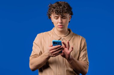 Akıllı telefondan internette sörf yapan yakışıklı bir erkek. Mavi arka planda gülücük ve neşe dolu bir adam. Teknoloji, başarı, mutluluk, sosyal ağ konsepti. Yüksek kalite
