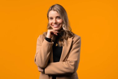 Dost canlısı beyaz sarışın kadın gülümsüyor, sarı stüdyoda mutlu kız portresi çiziyor. Güzel dalgalı saç stili, doğal makyaj. Yüksek kalite