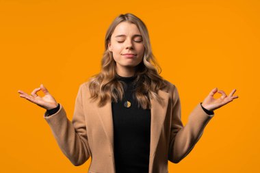 Sakin kadın rahatlıyor, meditasyon yapıyor, stresi reddediyor. Kadın derin nefes alıyor, sarı stüdyo arka planını sakinleştiriyor. Yoga, ahlaki denge, zen konsepti. Yüksek kalite