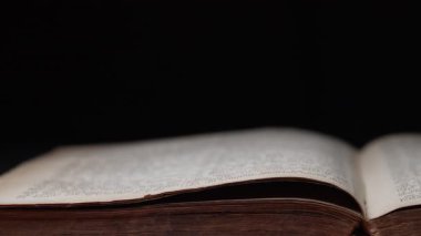 Kütüphanedeki masada Eski Açık Kitap 'ın yan görüntüsü. Eskimiş sayfalar, Kaypak. Siyah arka planda kadim yazılar. Edebiyat, yayın, eğitim. Yüksek kalite 4k görüntü