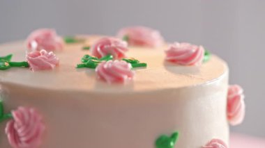 Güzel kremalı pasta döner tablada yavaşça dönüyor. Narin pembe çiçeklerle süslenmiş, beyaz kremalı yeşil yapraklar. Fırın, kutlama, düğün, pasta konsepti. Yüksek kalite 4k görüntü