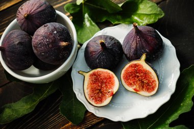 Beyaz tabakta yaprakları olan taze incir, kırsal ahşap masa. Ficus carica. Güzel mevsimlik meyveler, vejetaryen yemekleri. Üst Manzara. Yüksek kalite fotoğraf