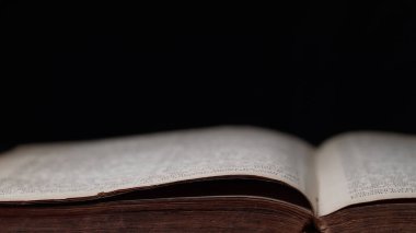 Kütüphanedeki masada Eski Açık Kitap 'ın yan görüntüsü. Eskimiş sayfalar, Kaypak. Siyah arka planda kadim yazılar. Edebiyat, yayın, eğitim. Yüksek kalite