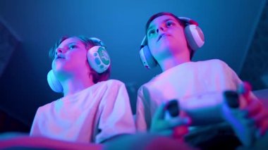 Oyuncuların arkadaşları oyun konsolunda joysticklerle oyun oynuyorlar. Oyun konsolu kullanan çocuklar, en yeni kablosuz oyun alanı. Hobi, e-spor, aile eğlencesi. 4k görüntü