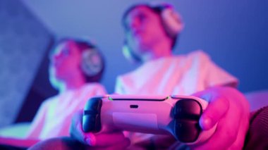 Çocuklar konsol TV 'de bilgisayar simülatörü oyunu oynuyorlar. Neon renkli odaları var. Oyun konsolu olan oyuncular, en yeni kablosuz oyun alanı. Hobi, e-spor. - Boş zaman. Yüksek kalite 4k görüntü