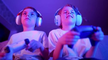 Çocuklar konsol TV 'de bilgisayar simülatörü oyunu oynuyorlar. Neon renkli odaları var. Oyun konsolu olan oyuncular, en yeni kablosuz oyun alanı. Hobi, e-spor. - Boş zaman. Yüksek kalite 4k görüntü