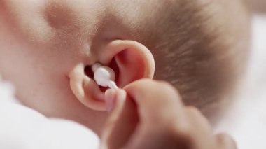 Anne, bebeğin kulağını pamuk tomurcuğuyla balmumundan temizliyor. Yeni doğan hijyen, sabah rutini. Bebek bakımı, yenidoğan kalitesinde 4K görüntü.
