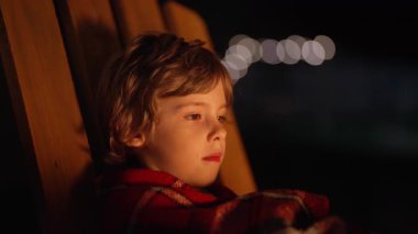 Küçük çocuk ışıltısından büyülenmiş titreyen ateşe bakıyor. Huzurlu bir an, çocuk, doğa, arka bahçedeki ateşin büyüsü. Yüksek kalite 4k görüntü