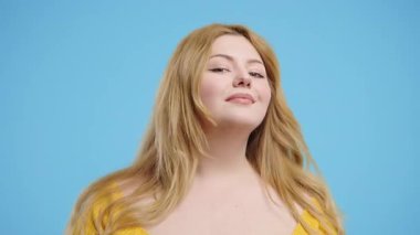 Artı, göz kırpan çapkın kadın mavi stüdyodaki kameraya gülümsüyor. Gerçek, doğal güzellik, hakiki Amerikan kadını, çeşitlilik, kapsayıcı kadın modeli. Yüksek kalite 4k görüntü