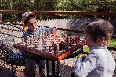 Öğrenci kardeşler tahta zeka oyunu oynuyorlar. Tahta satranç. Küçük çocuk oyunun temellerini öğreniyor. Piyon taşını hareket ettiriyor. Spor, başarı stratejisi kavramı