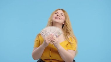 Zengin, aşırı kilolu, nakit parası olan bir kadını heyecanlandırdı. Mavi duvardaki Amerikan doları banknotları. İkramiyenin sembolü, kazanç, zafer, kazanan piyango. Yüksek kalite 4k