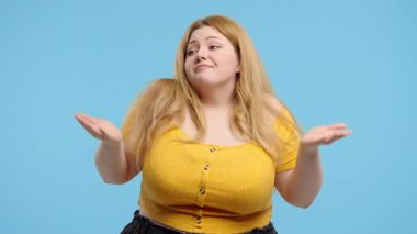 Vücut pozitifliği olan 30 'lu yaşlarda güzel bir kadın, omuzları kalkık, yardımcı olamıyor, bilemiyorum. Zor soru, suçlu tepkisi, mavi arka planda. Yüksek kalite 4k