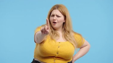 İlgisiz ve boyut olarak genç bir kadın dur işaretini onaylamıyor. Benimle oynama, bu kadar yeter. Mavi arka planda vücut pozitifliği olan kadın portresi. Yüksek kalite 4k