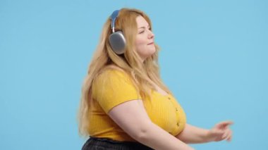 Mutlu artı beden kadınlar kafayı bulur, müzik dinler, mavi stüdyo arka planında kulaklıklarla dans etmekten zevk alır. Radyo, kablosuz modern ses teknolojisi, çevrimiçi çalar. Yüksek kalite 4k