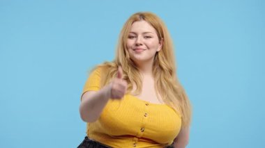 Artı el işareti olan boyunda bir kadın, baş parmak işareti gibi. Mutlu bayan, doğru seçim, harika bir anlaşma, mavi arka plan. Pozitif kadın model kameraya gülümser, onay, güven konsepti. 4k kalite