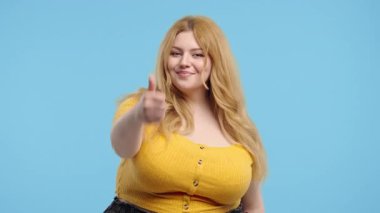 İri vücutlu, el işareti olan çekici bir kadın. Mutlu bayan, doğru seçim, harika bir anlaşma, mavi arka plan. Pozitif kadın model kameraya gülümser, onaylar, güvenilirdir.