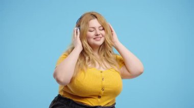 Mutlu artı beden kadınlar kafayı bulur, müzik dinler, mavi stüdyo arka planında kulaklıklarla dans etmekten zevk alır. Radyo, kablosuz modern ses teknolojisi, çevrimiçi çalar. Yüksek kalite