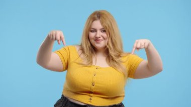 Vücut pozitifliği olan genç bir kadın reklam alanını işaret ediyor. Mavi arka plan. Blog yazarı aşağıdaki aboneliğe tıklamak istiyor. Ticari fikrin için yer kopyala, reklam içeriği. Yüksek kalite 4k