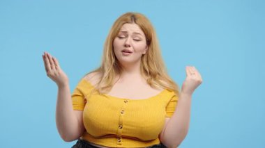 Canı sıkkın 20 'li yaşlarda, vücut pozitifliği olan, elleri mavi arka planda olan bir kadın öğrenci jesti. Boş vaatler, ironi, falan filan. Yalancı! Yüksek kalite 4k