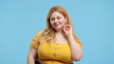 30 'lu yaşlarda aşırı kilolu bir kadın gülümsüyor, mavi stüdyo arka planında kameraya kur yapıyor. Sıradan kıyafetler içinde sevimli, neşeli bir bayan. Yüksek kalite 4k görüntü