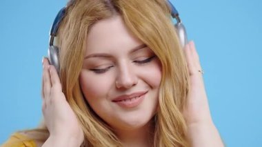 Mutlu artı beden kadınlar kafayı bulur, müzik dinler, mavi stüdyo arka planında kulaklıklarla dans etmekten zevk alır. Radyo, kablosuz modern ses teknolojisi, çevrimiçi çalar. Yüksek kalite 4k