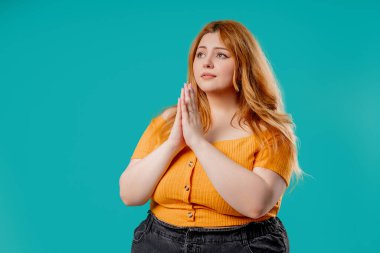 Mavi stüdyo arka planında dua eden çekici ve cüsseli bir kadın. Vücut pozitifliği olan kadın, birine arzularını tatmin etmesi için yalvarır, yardım eder, şans için dua eder. Yüksek kalite