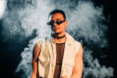  Güneş gözlüklü tuhaf kulüp üyesi gülümsüyor, neon ışıkta şık bir adam portresi çiziyor. Gece hayatı, yakışıklı Afrikalı Amerikalı adam. Yüksek kalite fotoğraf