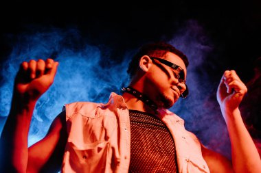 Şeffaf ağ gibi giyinmiş şık bir adam neon ışıkta dans ediyor, duman stüdyosunda ya da gece kulübünde. Kıvırcık saçlı seksi adamın portresi. Aktif enerji, ilham verici dans. Yüksek kalite fotoğraf