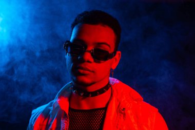 Dumanlı göz kamaştırıcı adam, neon yeşil ışık, gece kulübü. Sivri uçlu, siyah güneş gözlüklü seksi adamın portresi. Yüksek kalite fotoğraf