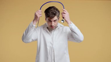 Beyaz önlüklü genç erkek doktor steteskop takıyor ve stüdyoda kameraya güvenle bakıyor. Tıbbi profesyoneller çalışmaya hazır, sağlık konsepti, modern ortamda portre. Yüksek kalite