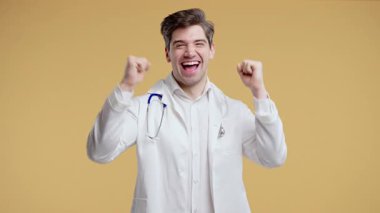 Doktor Dansı, olumlu duygular, mizah enerjisi, neşeli sağlık hizmetleri. Profesyonel beyaz önlüklü, Oyuncu Doktor sarı stüdyo arka planında izole edildi. Yüksek kalite 4k görüntü