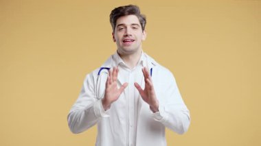 Beyaz önlüklü yetişkin bir erkek doktor kamerayla konuşuyor ya da video kaydediyor. Güvenilir sağlık sektörü profesyonel selamlama kitlesi, bej stüdyoda online toplantı sunumuna başlıyor.