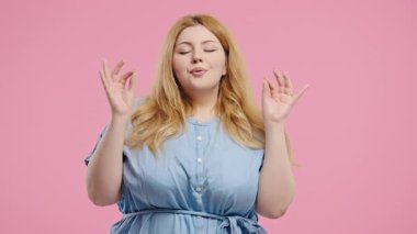 Sakin vücut pozitifliği olan kadın rahatlıyor, meditasyon yapıyor, stresi reddediyor. Artı boy kadın derin nefes alır, sakinleşir, pembe stüdyo arka planı. Yoga, ahlaki denge, zen konsepti. Yüksek kalite