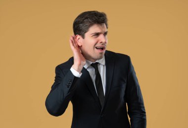 Stüdyo fotoğrafında resmi giyinmiş bir adam şaşkınlıkla tepki veriyor, duymadığı ve anlamadığı sinyalini veriyor. İletişim sorunları, yanlış duyma, teknik sorunlar, işyerindeki yanlış anlaşılmalar